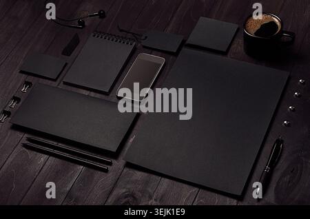 Black blank stationery set with phone, earphone, coffee on dark wood background, inclined. Stock Photo