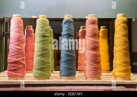 Row of colorful yarn spools and cones in pink, green, blue, and yellow on a textile factory loom machine. Stock Photo