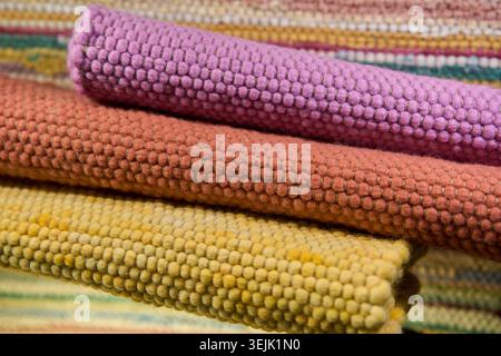Three rolled colorful woven cotton rugs in purple, orange, and yellow showing thick knobby textures. Stock Photo