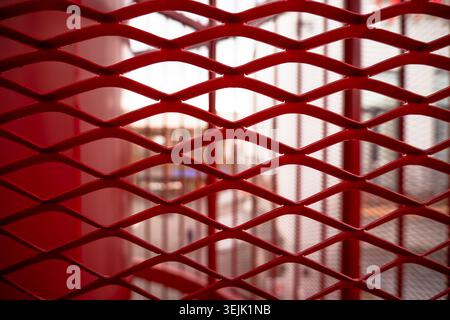 Abstract macro shot focusing on the diamond pattern of a painted red metal mesh fence with blurred background Stock Photo