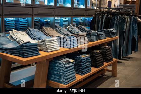 Rows of neatly folded blue and black denim jeans on a wooden display table inside a retail store Stock Photo
