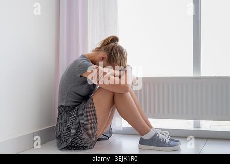 Sad woman sitting on the floor hugging her knees Stock Photo