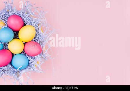 Easter festive background - yellow, blue, red eggs in paper blue nest  on pastel pink background with copy space, top view. Stock Photo