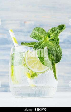 Mojito in wet glass with mint, slices lime, ice cubes, straw on soft blue background, closeup. Stock Photo