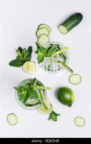 Summer cold drink with ice cubes, slices lime, cucumber, straw, twigs mint and ingredients on white wood board, top view. Stock Photo