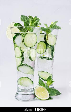 Mineral water with slices cucumber, ice, lime, mint on white wood table. Fresh summer cool fitness cocktail. Stock Photo