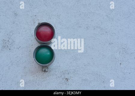 Small industrial traffic light with red and green lamps mounted on a grey textured wall. Stock Photo