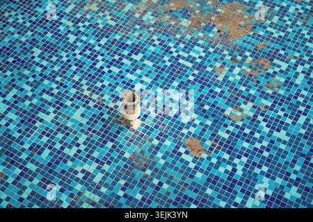 High angle view of textured small turquoise tiles inside a dry fountain or pool with a metal fixture Stock Photo