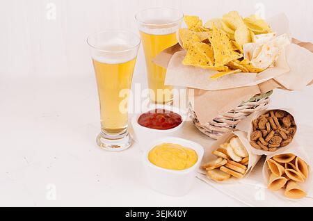 Different spicy mexican snacks and sauces - ketchup, curry - in bowl, cold lager beer on white wooden board. Stock Photo