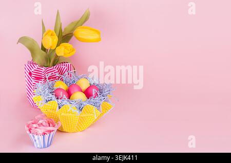 Springtime easter festive background - homemade painted multicolored eggs, tulips bouquet on pastel light pink background. Stock Photo