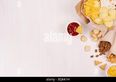 Fun fresh summer fast food background -  snacks  - nacho, croutons, chips, tortilla in craft paper cone and sauces on white wood Stock Photo