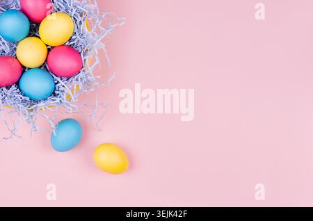Easter spring home decor - homemade painted multicolored eggs in pastel blue nest on light pink background. Stock Photo