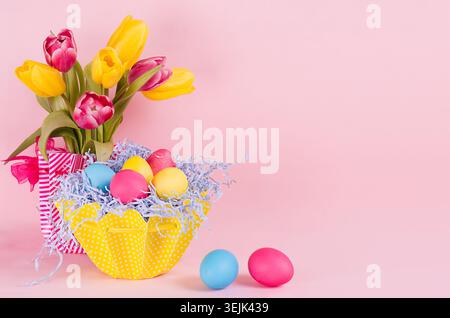 Easter spring home decor of yellow tulips, painted eggs, two eggs on pastel soft pink background. Stock Photo