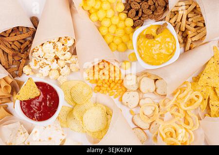Golden mexican colorful snacks - nachos, popcorn, croutons, chips in craft paper cone with red and yellow spiced sauces in bowls Stock Photo