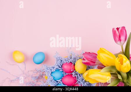 Springtime easter festive background - homemade painted multicolored eggs, tulips bouquet on pastel light pink background, top v Stock Photo