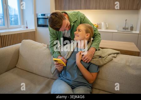 Cheerful couple man and woman enjoying time together at home, male partner showing care and love by covering lady in plaid while smiling female restin Stock Photo