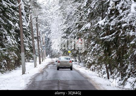 Car driving on frosty countryside road through spruce forest covered in snow on cold winter day. Stock Photo