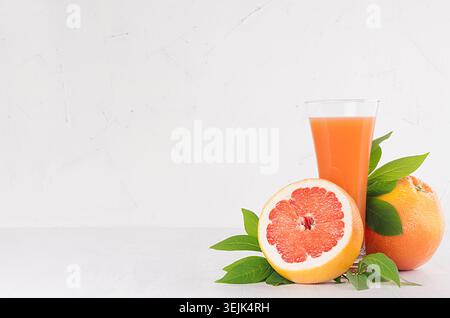 Ripe grapefruits with half slice, green leaves and juice on soft white modern kitchen interior. Healthy fruits summer background Stock Photo