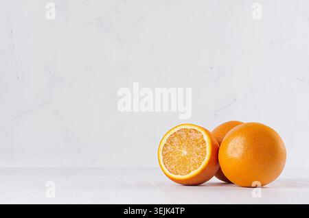 Three oranges and slice on white wood table and plaster background. Stock Photo