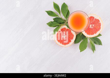 Ripe grapefruits with half slice, green leaves and juice on soft white wooden board, top view. Stock Photo
