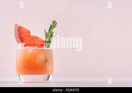 Cold grapefruit cocktail decorated twig rosemary and slice citrus on pink background. Stock Photo