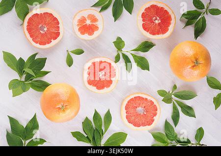 Slices grapefruit and green leaves on soft white wooden background, pattern, top view. Stock Photo