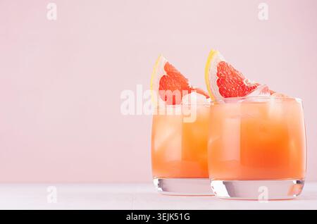 Cold grapefruit cocktail in two glasses with ice and pieces grapefruit on pastel pink background. Fresh summer healthy diet beve Stock Photo