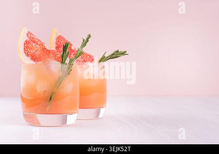 Summer cold cocktail with ice cubes, juice and slices grapefruit on pastel pink background. Stock Photo