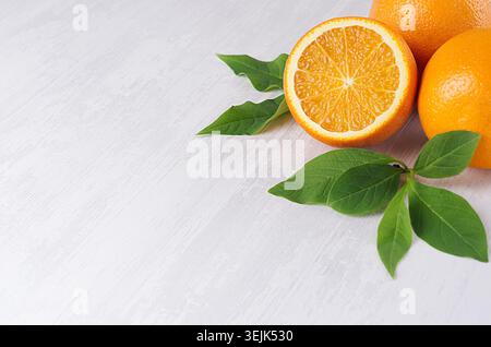 Juicy oranges with young green leaf and round slice closeup on soft white wood background. Stock Photo