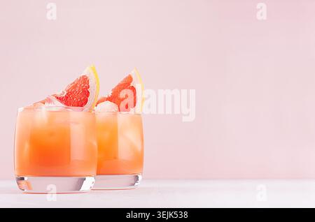Pink cocktail with ice cubes, juice and slices grapefruit on white wood board, copy space. Stock Photo