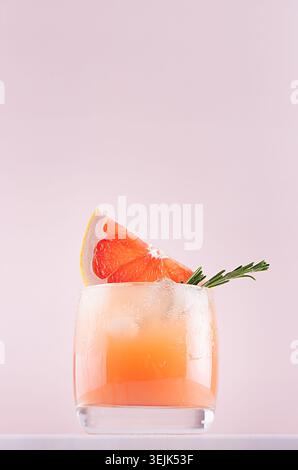Dieting detox water with grapefruit juice, ice cubes, green rosemary, sliced citrus on soft pastel pink and white background. Stock Photo