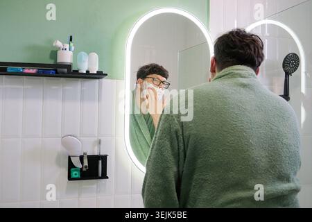 Man Shaving his Hair with Electric Razor in front of a Mirror Stock Photo