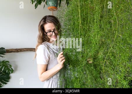 Happy young woman gardener hugging lush asparagus fern houseplant in flower store. Love of plants Stock Photo