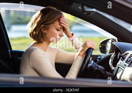 Exhausted woman driver feeling headache, sitting inside her car, keeping hand to head and feeling anxiety Stock Photo
