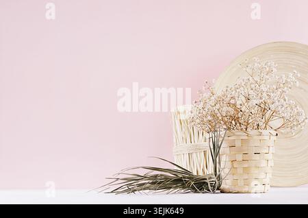 Small white dried flowers in beige wicker basket and wooden decor on soft pink pastel background. Stock Photo