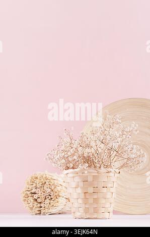 Gentle spring vanilla background with white dry flowers and bamboo dish on light table and pink wall. Stock Photo