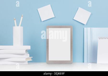 Modern style workplace - white stationery, blank tablet computer on soft blue background and light desk. Stock Photo