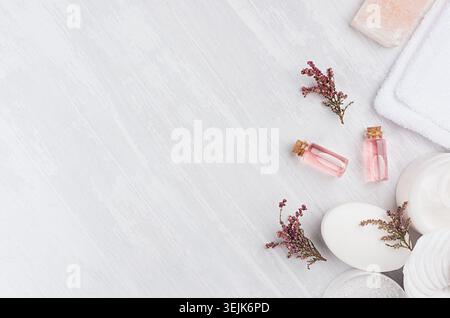 Natural spa cosmetics with pink rose oil, salt, soap and lavender flowers on white wood background, top view, border. Stock Photo