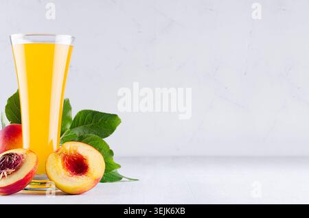Vegetarian dieting drink - ripe fresh nectarines, green leaves and juice in elegante glass on white modern kitchen wood table. Stock Photo