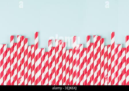Red striped cocktail straws on pastel mint color as abstract joyful background, border with copy space. Stock Photo