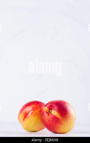 Fresh juicy nectarines on light white wooden board, vertical. Fresh summer season background. Stock Photo