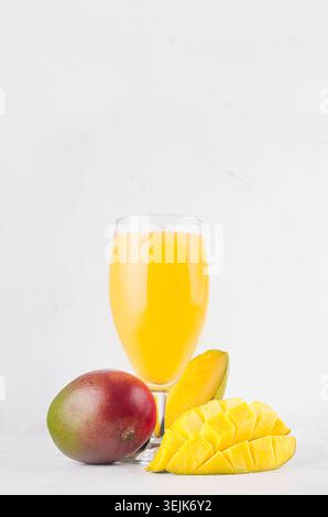 Bright colorful yellow fruits beverage of mango with sliced half closeup on soft white wood table, vertical. Stock Photo