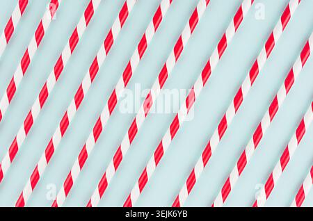 Red striped cocktail straws on pastel mint color as abstract joyful background, diagonal lines pattern. Stock Photo