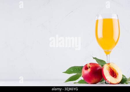 Fresh peach juice in elegance glass  and ripe red nectarines with green leaves  on soft white wood board. Sweet summer fruits an Stock Photo