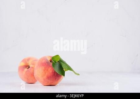 Two big ripe peaches with green leaves on white light wooden table, copy space. Stock Photo