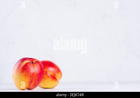 Red ripe two nectarines on soft light white wood background with copy space. Healthy food backdrop. Stock Photo