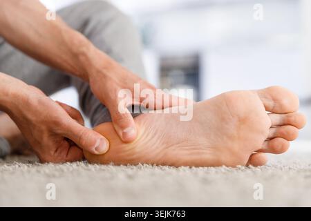 Man hands giving foot massage to yourself after a long walk, suffering from pain in heel spur, close up, indoors. Flat feet, leg fatigue, plantar fasc Stock Photo