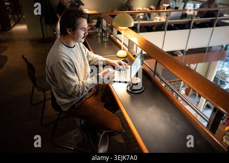 Positive relaxed businessman working on remote using laptop in trendy co-working cafe space. Stock Photo
