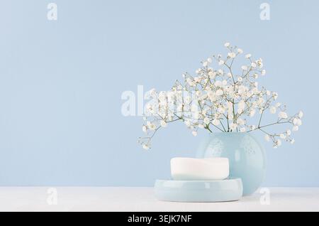 Bathroom interior - ceramic accessories - light blue circle vase, soap with white flowers on white wood table. Stock Photo