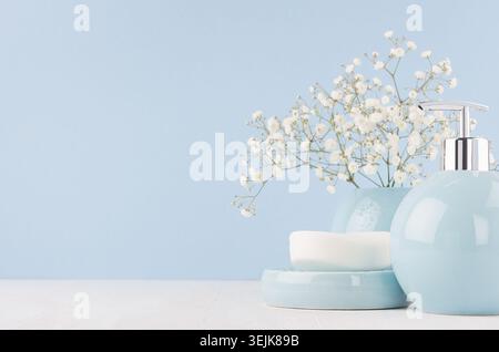 Bathroom interior - ceramic accessories - light blue circle vase with white flowers, soap dispenser  on white wood table. Stock Photo